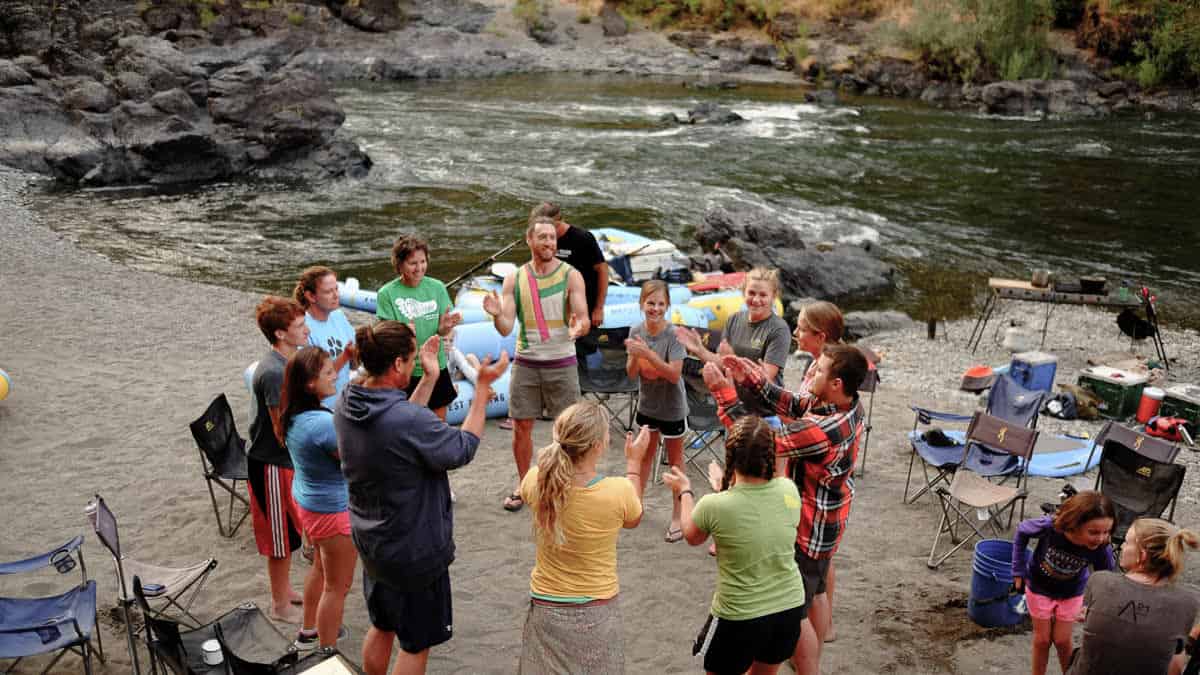 A group plays a game at camp alongside the Rogue River.